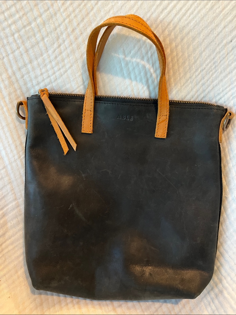 Minimalist Black leather Able bag with brown handle and strap.